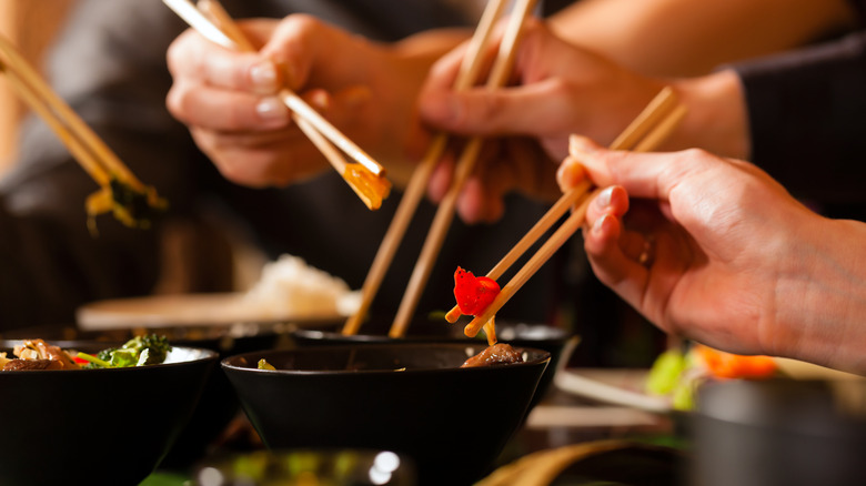 Multiple hands hold chopsticks over bowls