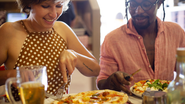 woman eating pizza while table mate eyes her plate