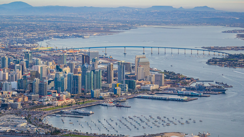 Birds eye view of downtown San Diego buildings and high-rises, boats on the water, and a long bridge.