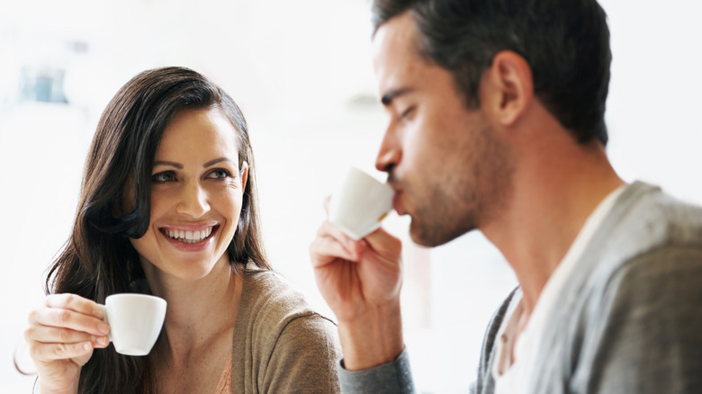 A woman smiles at a man drinking espresso