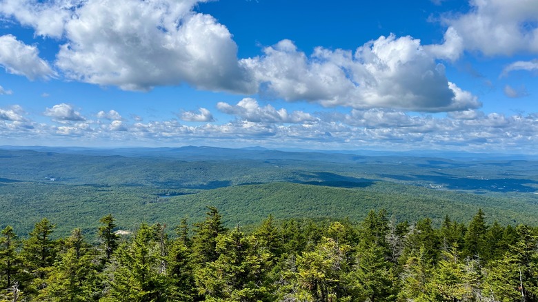 View from the top of a mountain summit overlooking green hills with clouds in the blue sky