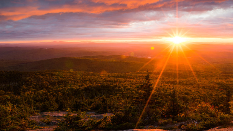 A colorful sunset view from the top of a mountain summit over forests below