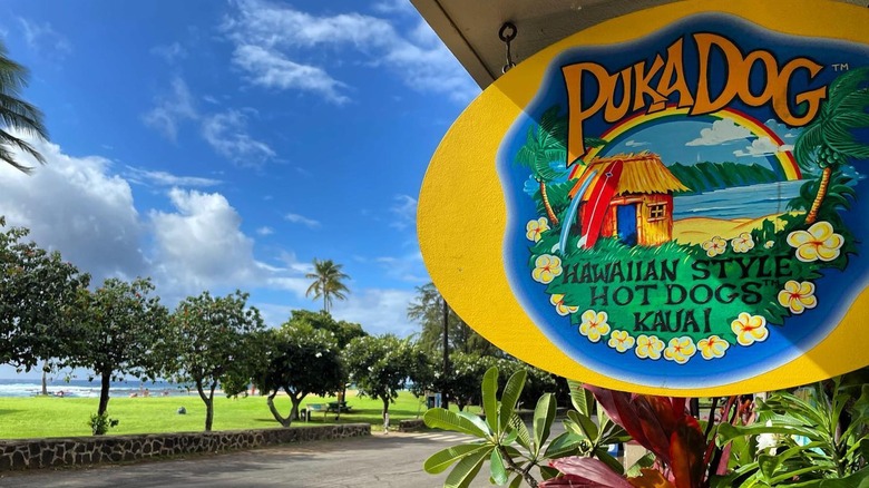 Puka Dog sign with park, trees, and sky in background