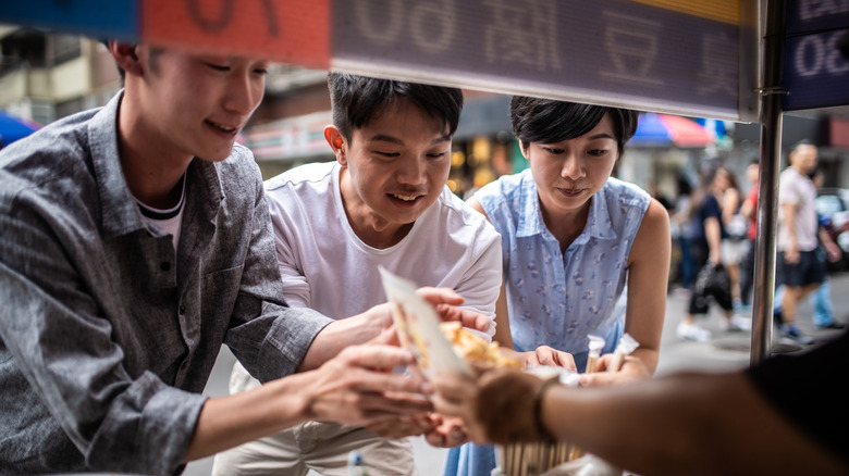 Three people ordering streetfood from a vendor