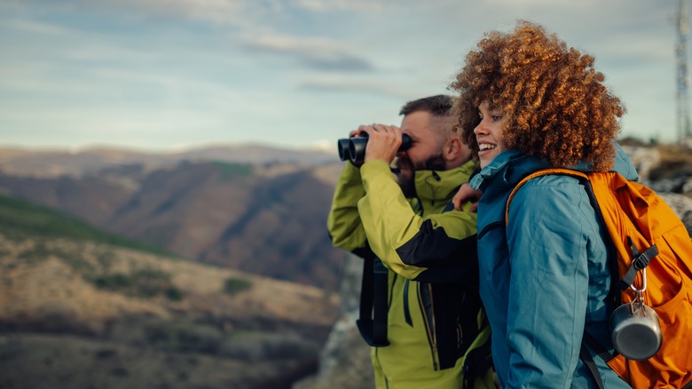 two hikers with one using binoculars to look at mountain view