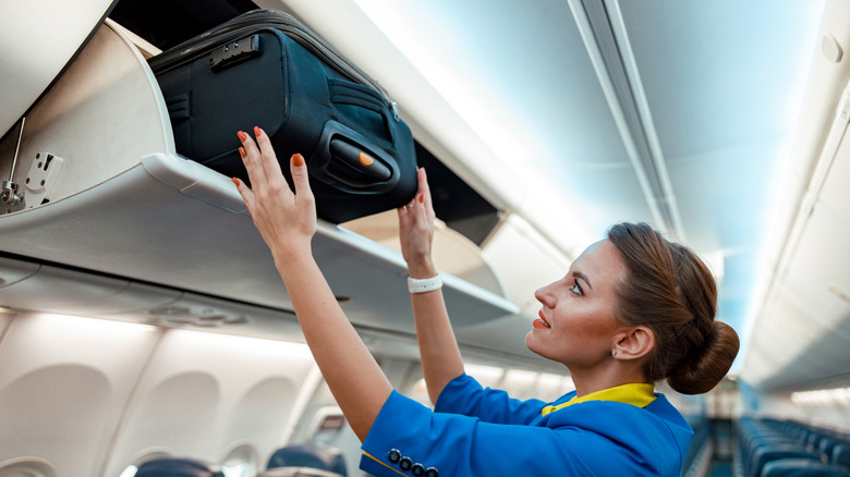 Flight attendant placing travel bag in airplane