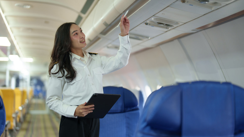 Flight attendant inspecting the luggage racks on airplane