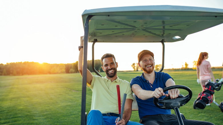 Two men in a golf cart smiling