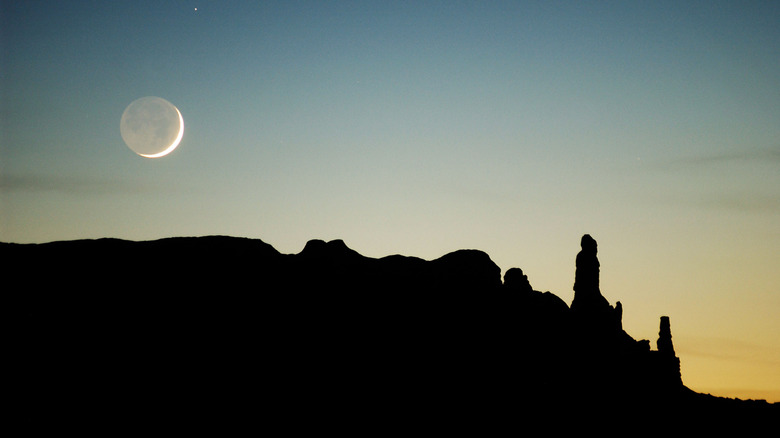Moon over silhouette of desert rocks at dusk
