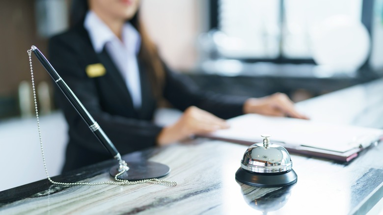 hotel employee standing at front desk with a pen and a bell
