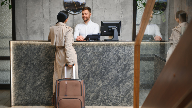 A woman in a trench coat checks into a hotel