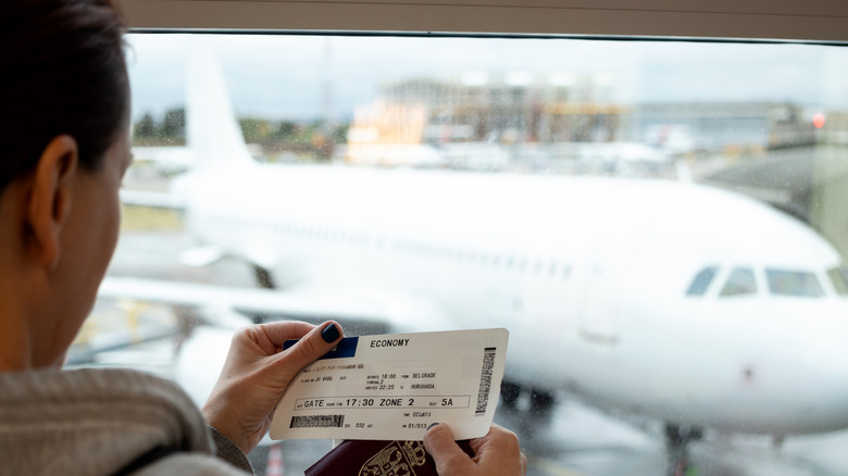 A woman holding her passport and economy boarding pass