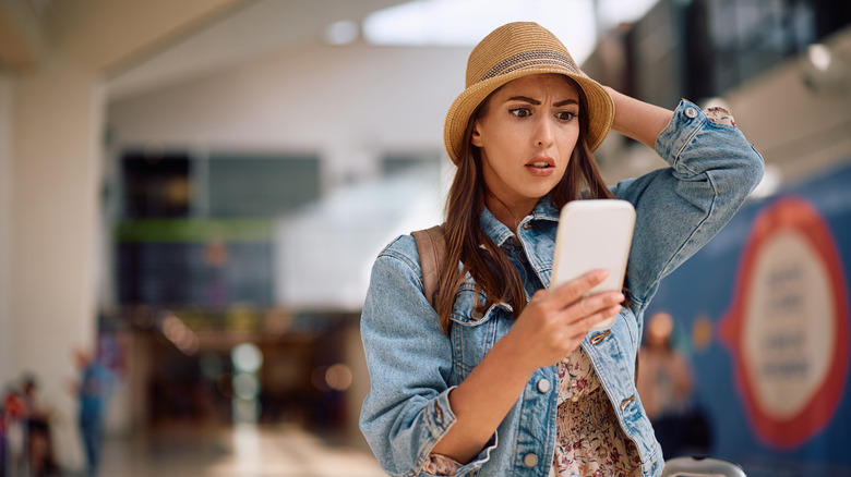 A shocked woman looking at her phone in the airport
