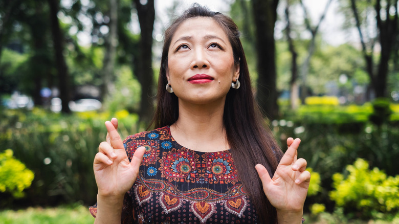 A woman with long dark hair looking up and crossing her fingers