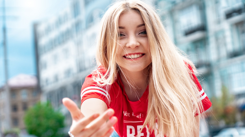 A blonde woman looking at the camera and beckoning with her hand