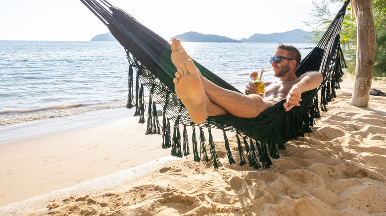 Man enjoys a refreshing drink while lounging in a hammock on a sunny beach