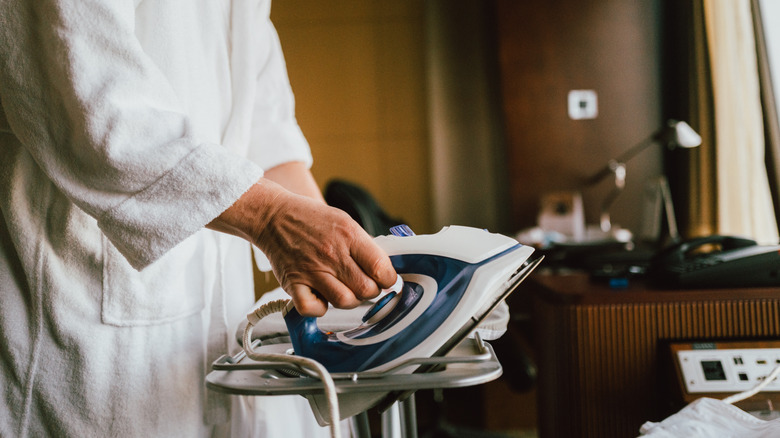 A hotel guest in a bathrobe irons clothes