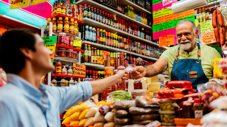A man hands a vendor a peso note at a market stall in Mexico