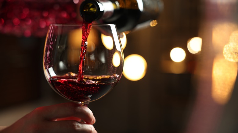 A hand holds a glass by the stem as wine is poured