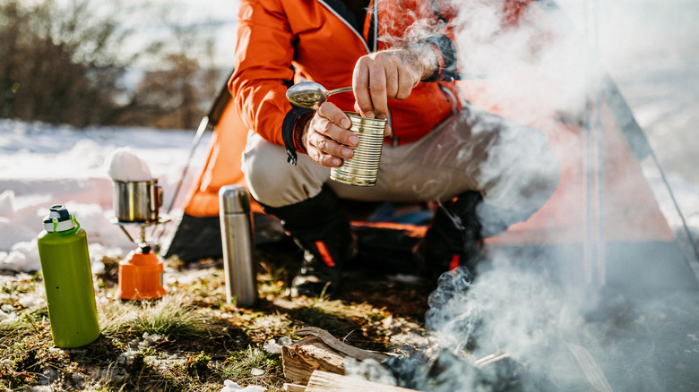 A camper opens a can of food on a snowy winter day.