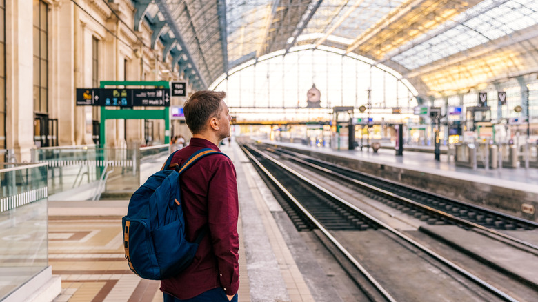 A young man wearing a backpack waiting on a train platform