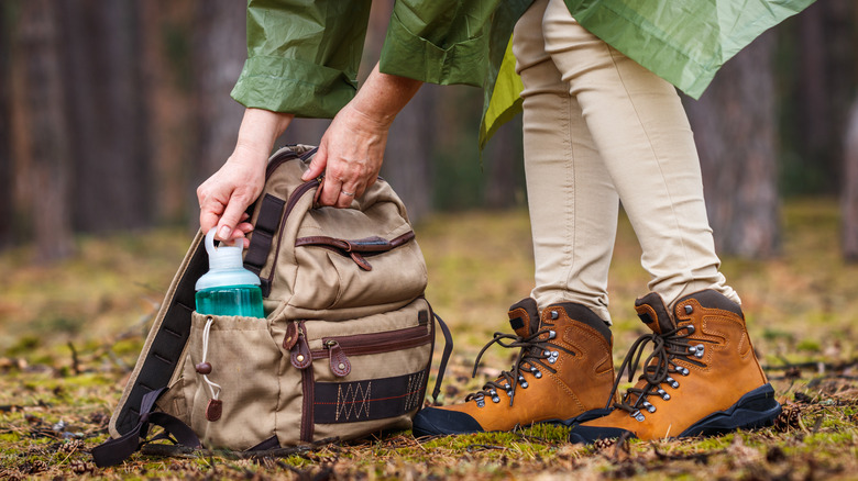 A person wearing hiking boots holding backpack and water bottle