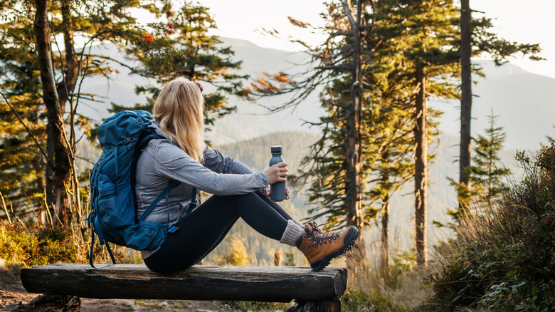 Hiker with backpack relaxing on a bench while holding water bottle