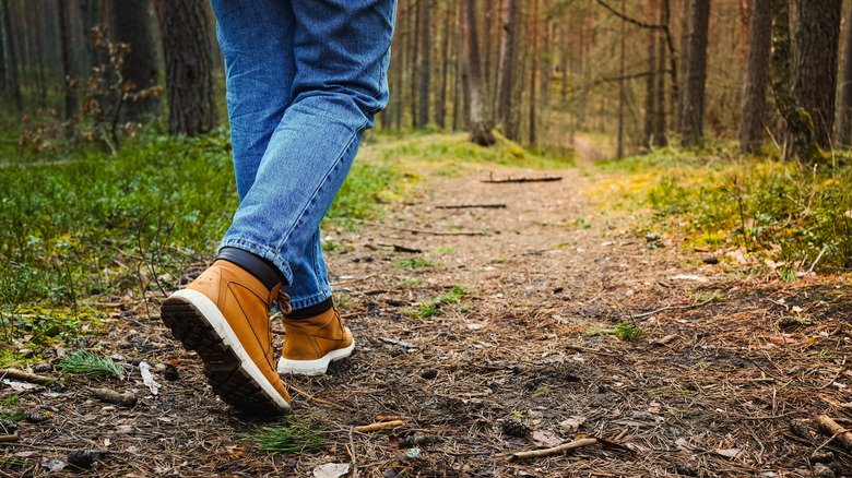 Closeup of person's feet hiking through forest in jeans and boots