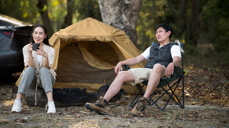 Woman and man relaxing in front of tent, woman holding mug in hand