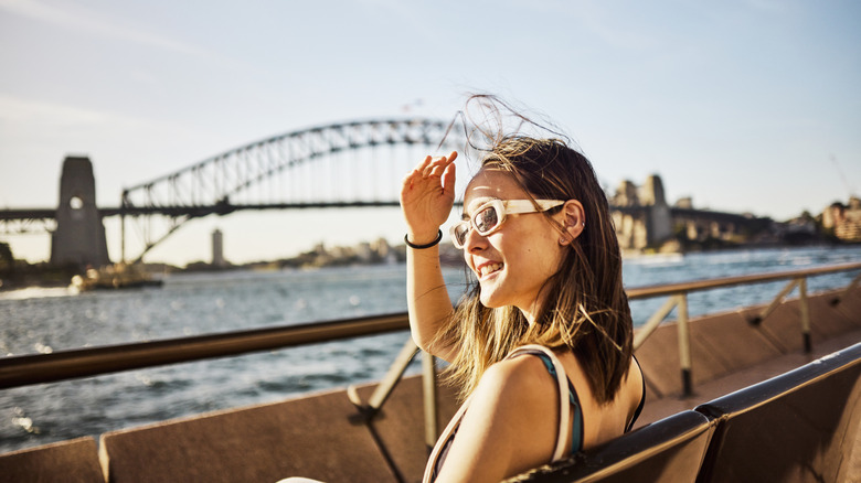 An Asian solo traveler sits admiring the breathtaking sea view of Sydney's cityscape.