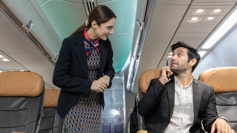 A flight attendant speaks to a man on his phone.