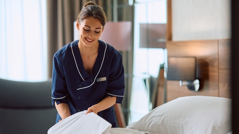 smiling hotel housekeeper making bed