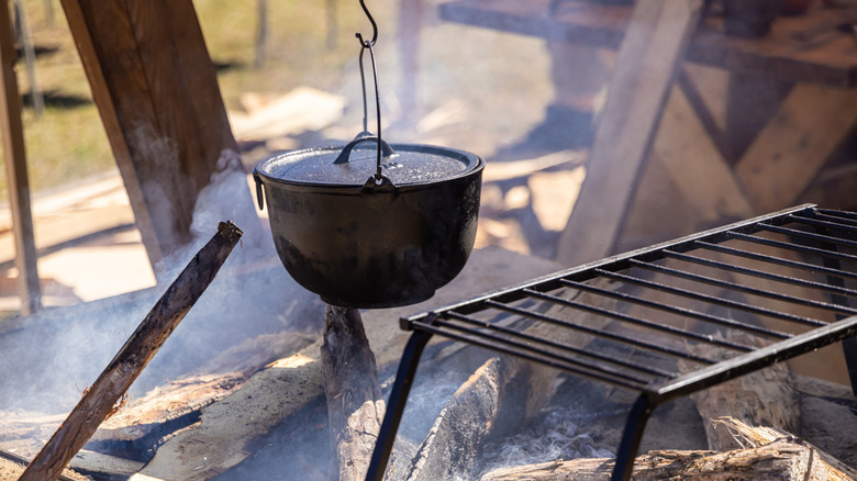 A Dutch oven is suspended over a campfire from a hook