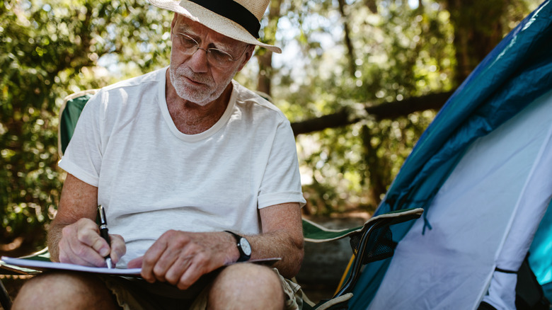 an older man sitting in front of a tent writing a book