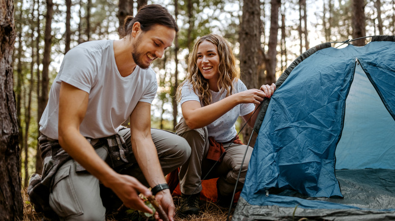 cheerful man and woman setting up tent in forest