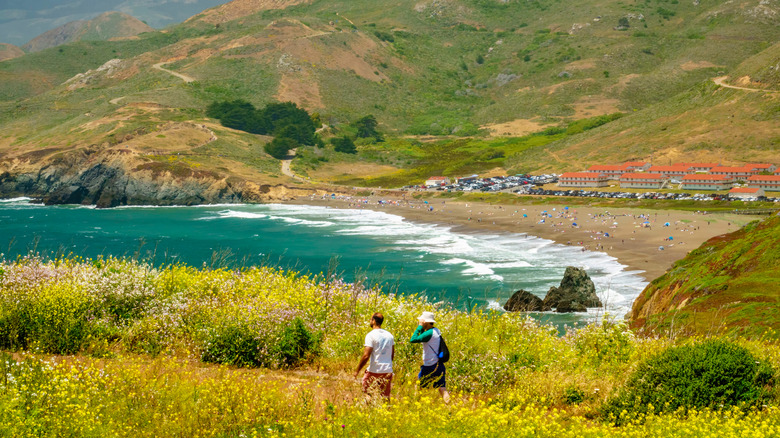 two hikers walking through wildflowers with fort Cronkhite and Rodeo Beach in the background