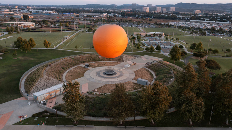 A giant orange hot air balloon at the center of a complex of sports fields