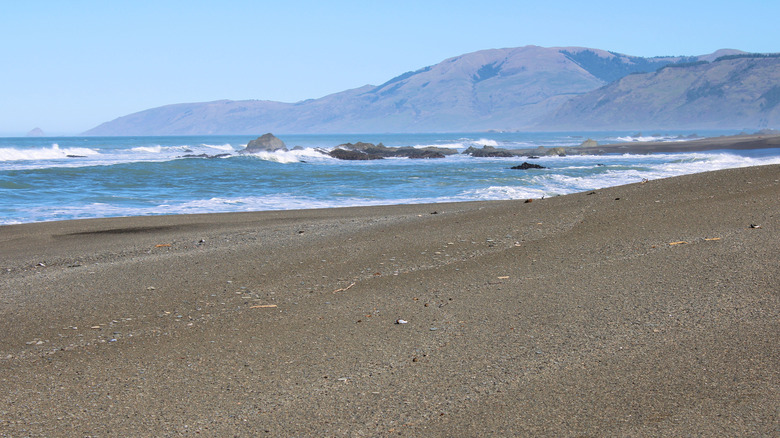 Waves crashing onshore to a sandy beach surrounded by coastal mountains and the Pacific Ocean taken on the Northern California Coast at a black sand beach in the Lost Coast, CA