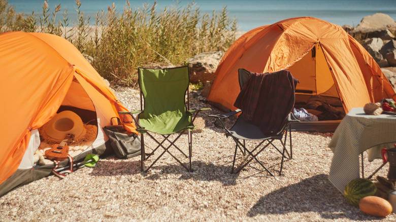 Two empty camping chairs set up by orange tents at a beachside campsite