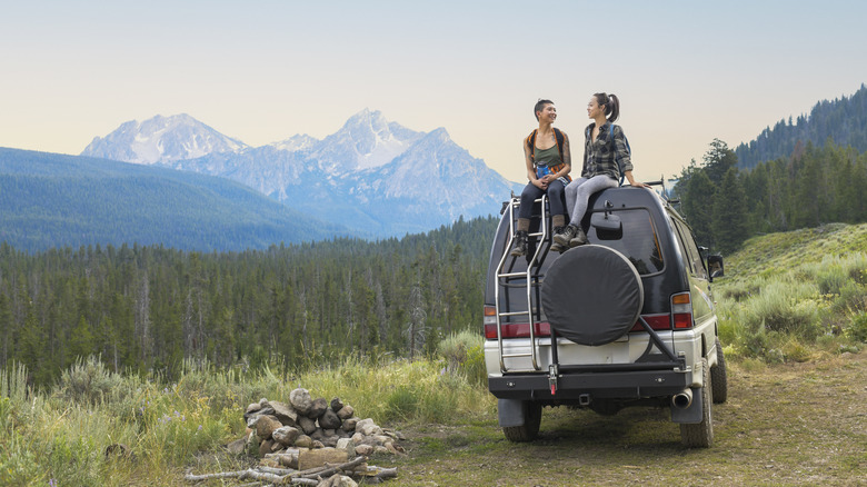 Two female friends sitting on a camper van in a forest park