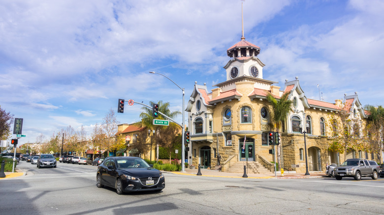 Cars driving past the honey-colored Old City Hall in Gilroy, which is topped with a clock tower