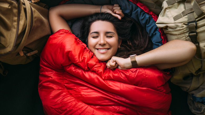 A smiling woman lies in her sleeping bag
