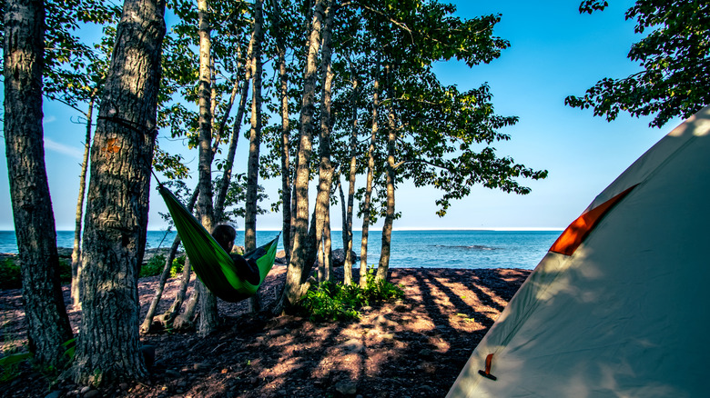 A man in a hammock next to a tent in front of Lake Superior