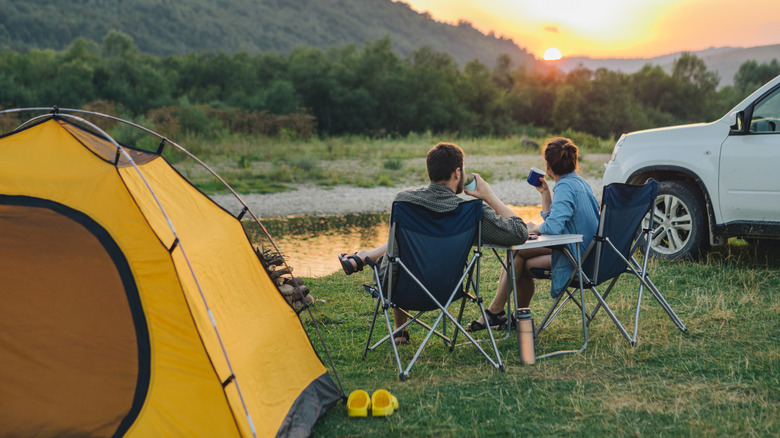 Two campers sitting in chairs watching a sunset along a riverbed.