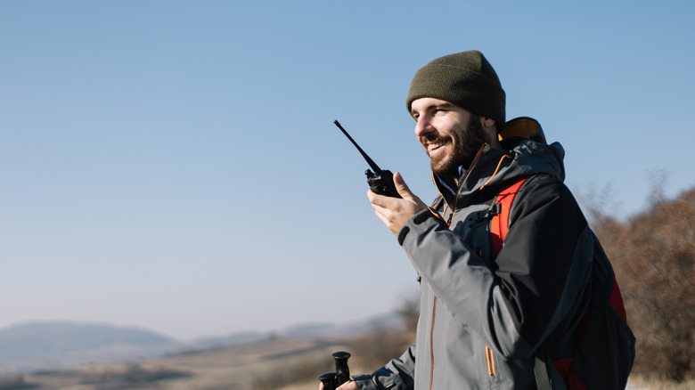 Smiling man hiking using a two-way handheld radio.
