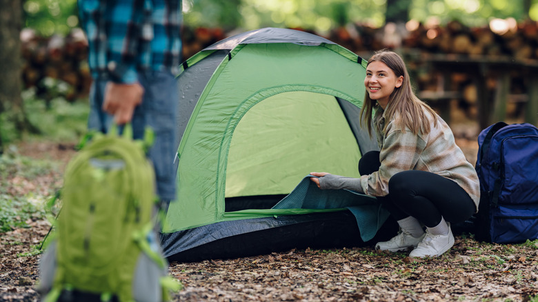 A woman squatting and smiling next to her tent.