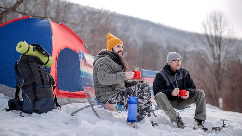 Two men sitting on chairs in front of a tent in the snow.
