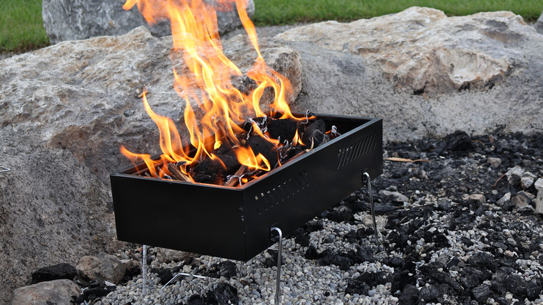 An elevated black box fire pit with flames around rocks and charcoal stones.