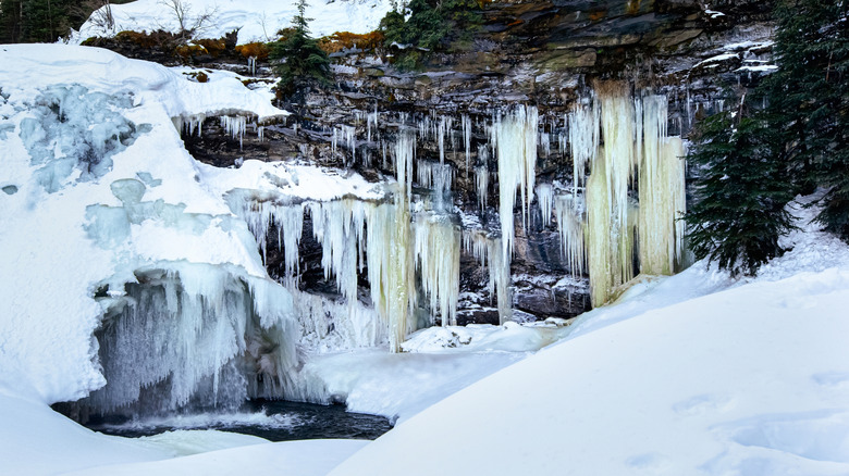 Frozen waterfalls with long icicles hanging from rocks to the ground covered with snow.