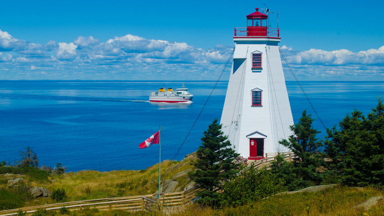 Swallowtail Lighthouse with a ferry passing near a Canadian flag on the edge of Grand Manan Island in New Brunswick on a sunny day